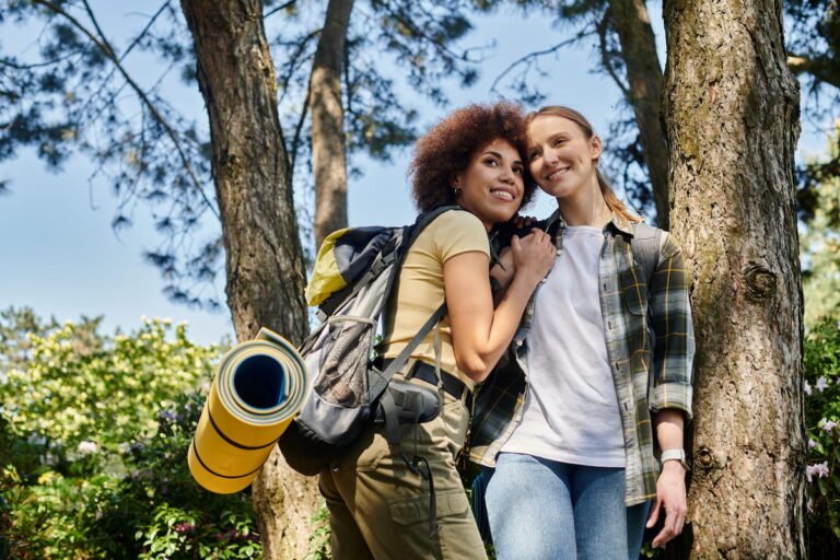Two smiling backpackers carrying a rolled sleeping mat while walking through a wooded trail