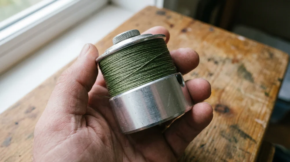 A spinning reel spool filled with green braided line, held in one hand